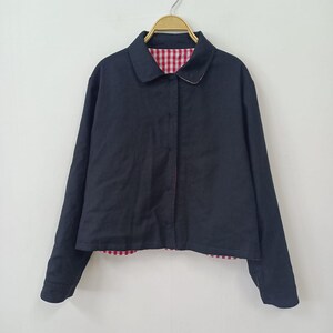 May include: A navy blue jacket with a classic collar and long sleeves. The jacket features a red and white gingham lining visible at the collar and hem. The jacket is hanging on a gold hanger.
