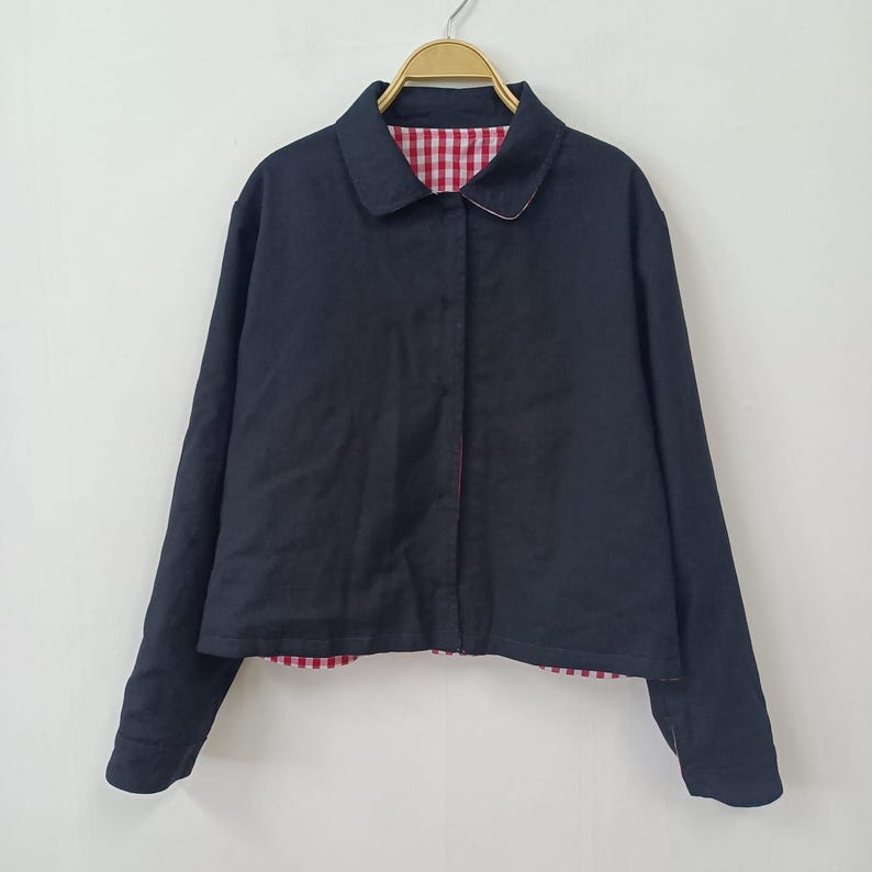 May include: A navy blue jacket with a classic collar and long sleeves. The jacket features a red and white gingham lining visible at the collar and hem. The jacket is hanging on a gold hanger.