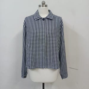 Op de afbeelding: Een zwart-wit geruit jasje met lange mouwen en een kraag. De jas is in het midden geknoopt en wordt op een mannequin getoond. Het patroon is een klassiek ruitontwerp.