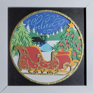 May include: A red and gold sleigh with a gold glitter border, surrounded by a winter scene with a Christmas tree, reindeer, and the words "Believe" in a whimsical font. The scene is set against a blue sky with white stars.