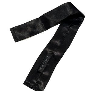 Può includere: Una maschera per dormire in raso nero con la scritta "EDGE SILKS" stampata sul lato.