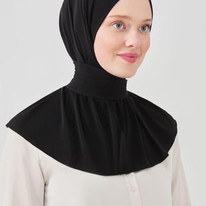 May include: A black jersey knit hijab with a high neck and a wide, flowing collar. The hijab is made of a soft, stretchy fabric and is designed to be comfortable and easy to wear.