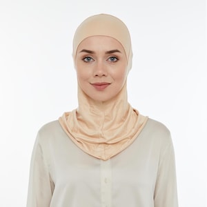 May include: A light beige seamless hijab with a turtleneck style. The hijab is made of a soft, stretchy fabric.