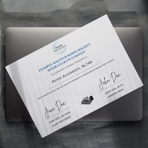 May include: A white certificate with blue text, featuring the text "EXAMPLE AMATEUR RADIO SOCIETY INTER-CLUB CW CONTEST" and the name "PETER ALEXANDER, NL7AK". The certificate is on a gray laptop.
