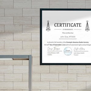 May include: A framed certificate of membership with the text "CERTIFICATE OF MEMBERSHIP" and the name "John Doe, KFIXXX". The certificate is for the Example Amateur Radio Society, dated September 19, 2025. The certificate has a black frame.