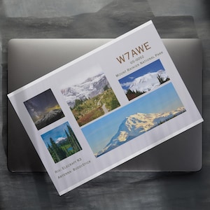 Puede incluir: Una postal con imágenes del Parque Nacional Mount Rainier, con el texto "W7AWE US-0052 Mount Rainier National Park". La postal está sobre un portátil cerrado.