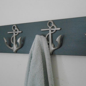 May include: A wooden wall-mounted coat rack with four silver anchor hooks. A light blue towel is hanging on one of the hooks.