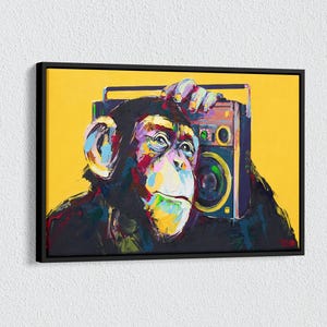 May include: A framed canvas art print featuring a colorful chimpanzee holding a vintage boombox. The artwork has a yellow background and a black frame. The chimpanzee's face is painted with vibrant colors.