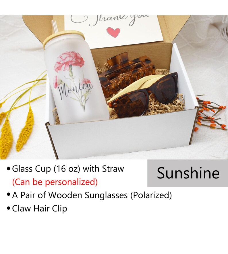 May include: A white gift box containing a personalised glass cup with a straw, a pair of wooden sunglasses, and a brown claw hair clip. The box is labelled "Sunshine".