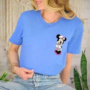 Puede incluir: Camiseta azul claro con un dise&ntilde;o de dibujos animados de Minnie Mouse. El gr&aacute;fico de Minnie Mouse es en negro, blanco, rosa y gris. La camiseta tiene mangas cortas y cuello redondo.