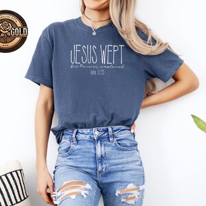 May include: A blue t-shirt with the text "JESUS WEPT" in white script, with the text "but He never complained" and "John 11:35" below. The shirt is paired with blue jeans.