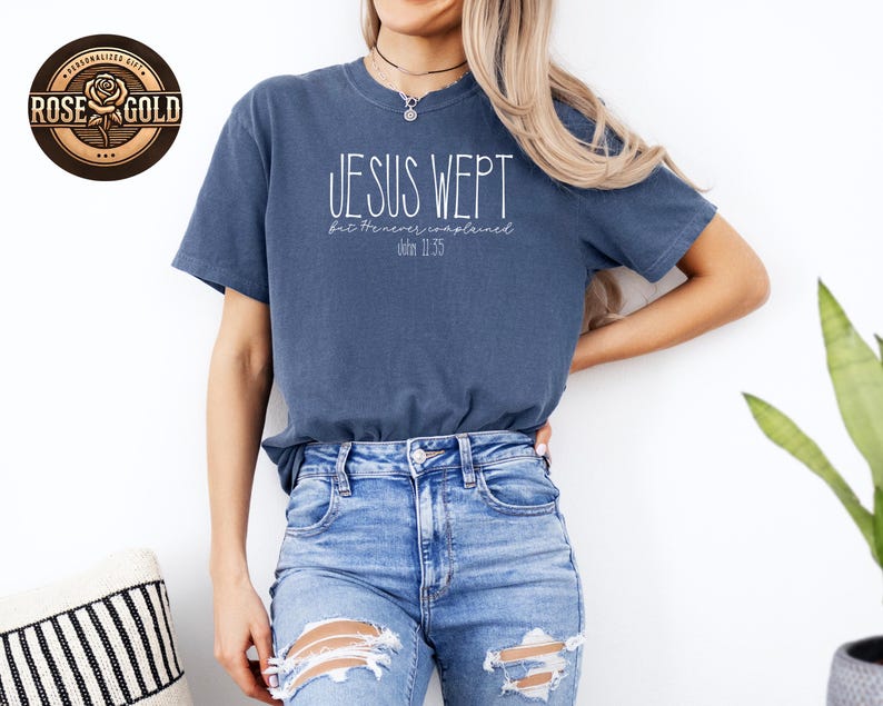 May include: A blue t-shirt with the text "JESUS WEPT" in white script, with the text "but He never complained" and "John 11:35" below. The shirt is paired with blue jeans.
