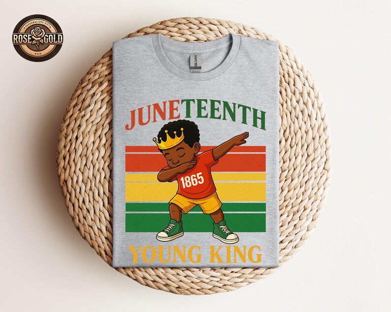Puede incluir: Una camiseta gris con una ilustraci&oacute;n de dibujos animados de un ni&ntilde;o negro joven haciendo dab, con una corona y el n&uacute;mero 1865. La camiseta tiene las palabras "Juneteenth" y "Young King" en un dise&ntilde;o colorido.