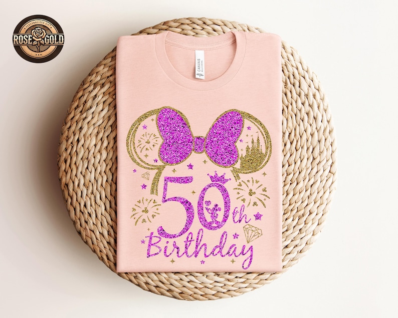 May include: A light pink t-shirt featuring a glittery purple bow and mouse ears design. The shirt has the text "50th Birthday" in a glittery purple font, with fireworks and a diamond graphic.