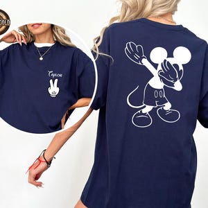May include: Navy blue t-shirt with a white Mickey Mouse graphic on the back and a peace sign with the name "Taylor" on the front. The shirt has a relaxed fit and a crew neck. The design is a playful and casual style.