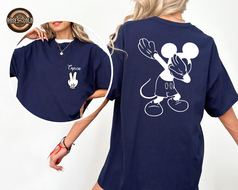 May include: Navy blue t-shirt with a white Mickey Mouse graphic on the back and a peace sign with the name "Taylor" on the front. The shirt has a relaxed fit and a crew neck. The design is a playful and casual style.