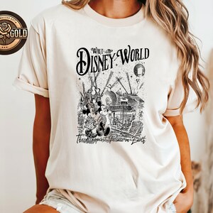 May include: A cream-coloured t-shirt with a black and white graphic of Mickey and Minnie Mouse at Walt Disney World. The design includes the words "Walt Disney World" and "The Happiest Place on Earth."