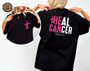 May include: Black t-shirt with a pink cross and ribbon design on the front. The back of the shirt features the words "HEAL CANCER" in pink glitter and white text, with the Bible verse Luke 1:37.