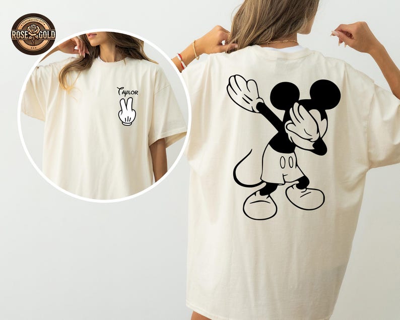May include: Cream-coloured t-shirt with a black and white Mickey Mouse graphic on the back, covering his eyes. The front of the shirt has the word "Taylor" and a hand gesture.