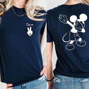 May include: Navy blue t-shirt featuring a white Mickey Mouse design on the back and the name "Taylor" with a peace sign on the front. The top is a short-sleeved crew neck.