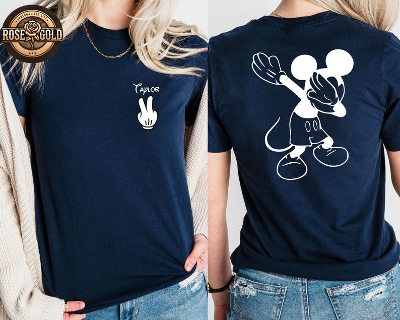 May include: Navy blue t-shirt featuring a white Mickey Mouse design on the back and the name "Taylor" with a peace sign on the front. The top is a short-sleeved crew neck.