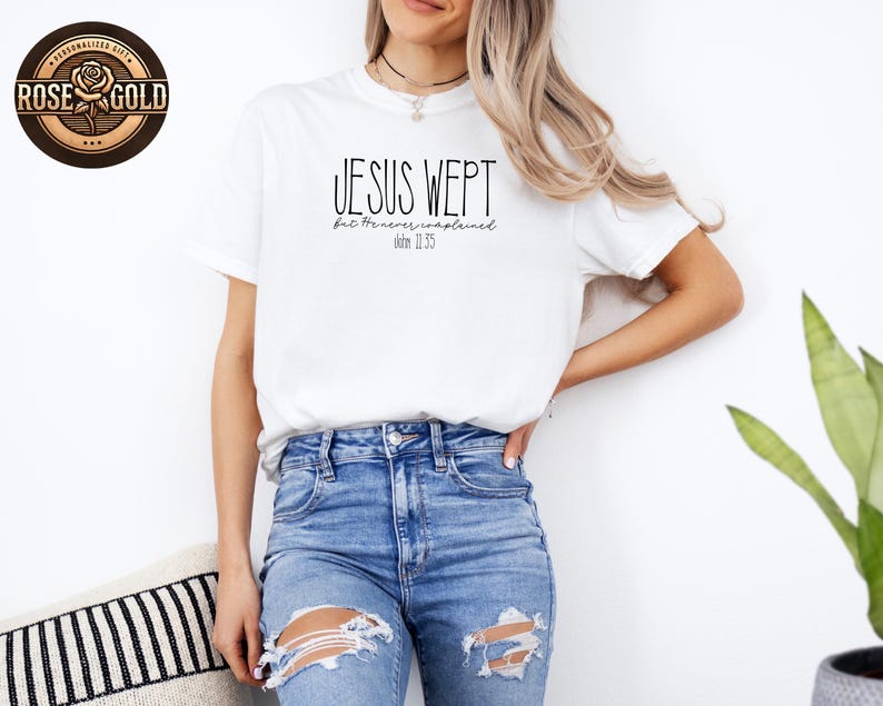 May include: White t-shirt with the text "JESUS WEPT" in black, with "but He never remained" and "John 11:35" below. The shirt is worn with blue jeans. A "Rose Gold" logo is visible in the upper left corner.
