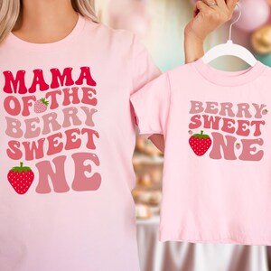 May include: Matching pink t-shirts with strawberry graphics and text. One shirt says "MAMA OF THE BERRY SWEET ONE" and the other says "BERRY SWEET ONE". The shirts are a light pink color.