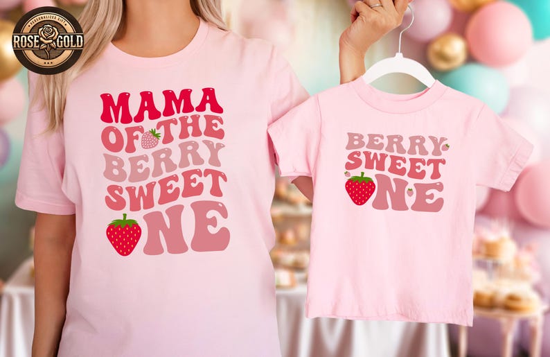 May include: Matching pink t-shirts with strawberry graphics and text. One shirt says "MAMA OF THE BERRY SWEET ONE" and the other says "BERRY SWEET ONE". The shirts are a light pink color.
