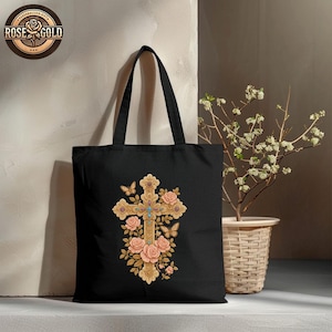 May include: Black tote bag featuring a detailed gold cross design adorned with pink roses, butterflies, and turquoise accents. The bag has long handles and the text "ROSE GOLD" in a circular logo.