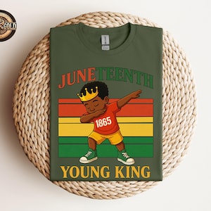 Puede incluir: Camiseta verde oliva con la palabra "Juneteenth" en rojo y verde. La camiseta muestra una ilustraci&oacute;n de dibujos animados de un joven negro haciendo un dab, con una corona y el n&uacute;mero "1865" en su camisa. Las palabras "Young King" est&aacute;n debajo.