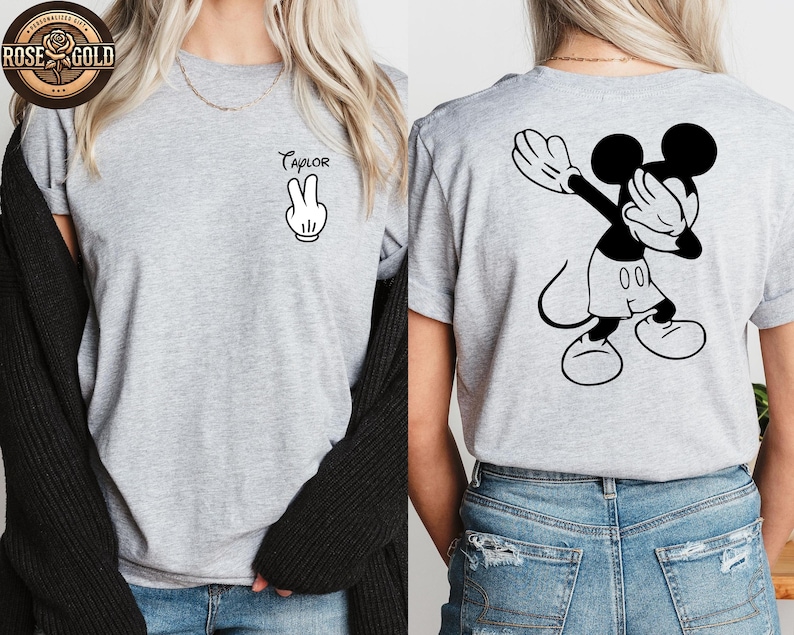 May include: A light grey t-shirt with a black and white Mickey Mouse design. The front displays the name "Taylor" above a peace sign hand gesture. The back of the shirt features Mickey Mouse doing a dab pose.