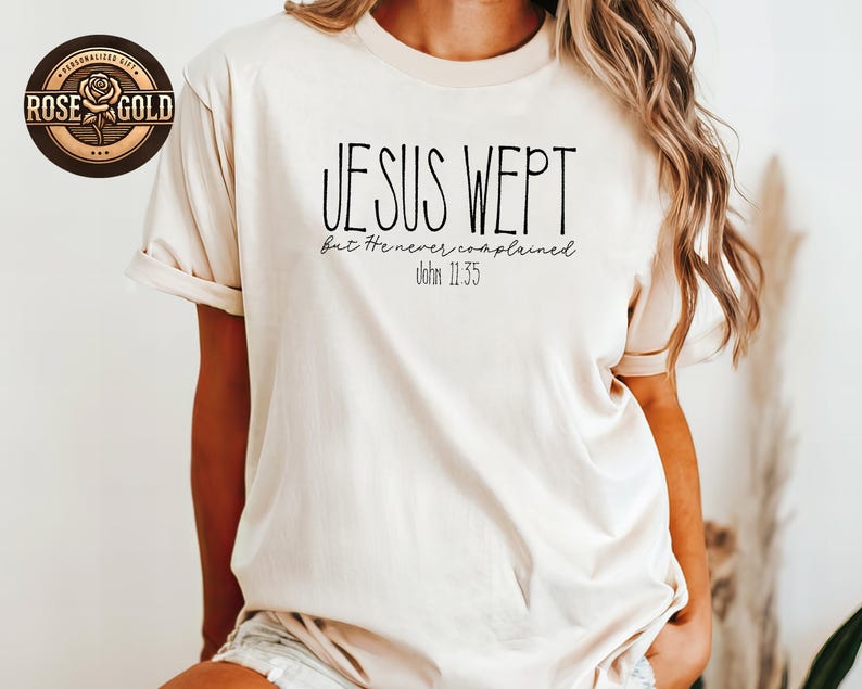 May include: A beige t-shirt with the text "JESUS WEPT but He never complained John 11:35" in black. The shirt has short sleeves and a relaxed fit. A rose gold sticker is visible in the upper left corner.