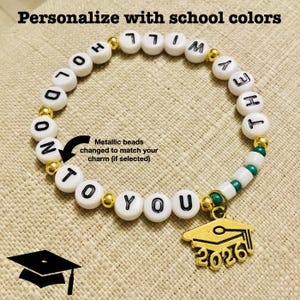 May include: A white beaded bracelet with black lettered beads spelling "HOLD ON TO YOU, Whitney Hey". The bracelet has gold metallic beads and a gold graduation cap charm with "2026" on it. The text "Personalise with school colours" is at the top.