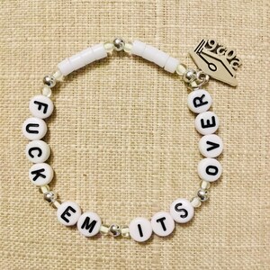 May include: White beaded bracelet with the words "FUCK EM ITS OVER" spelled out in black letters. The bracelet includes silver beads and a silver charm with a pen and the number "2020".