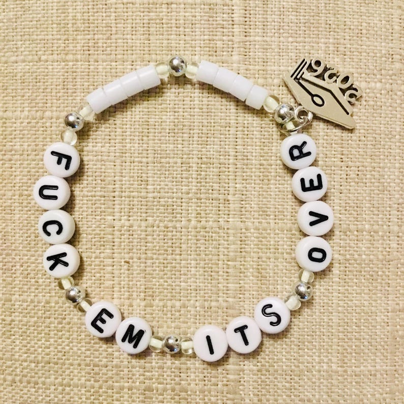 May include: White beaded bracelet with the words "FUCK EM ITS OVER" spelled out in black letters. The bracelet includes silver beads and a silver charm with a pen and the number "2020".