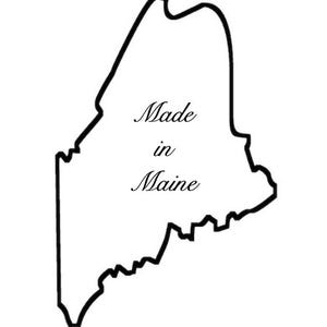 May include: A black and white outline of the state of Maine. The words "Made in Maine" are written in a cursive font inside the state's borders. The image is on a white background.