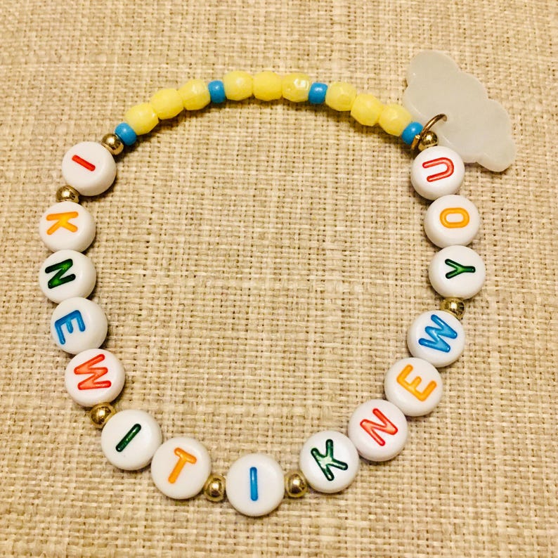 May include: A beaded bracelet featuring white round beads with colorful letters spelling I KNEW IT I KNEW YOU, interspersed with small gold-tone metallic beads. The top section includes yellow faceted beads, blue beads, and a white cloud-shaped charm.
