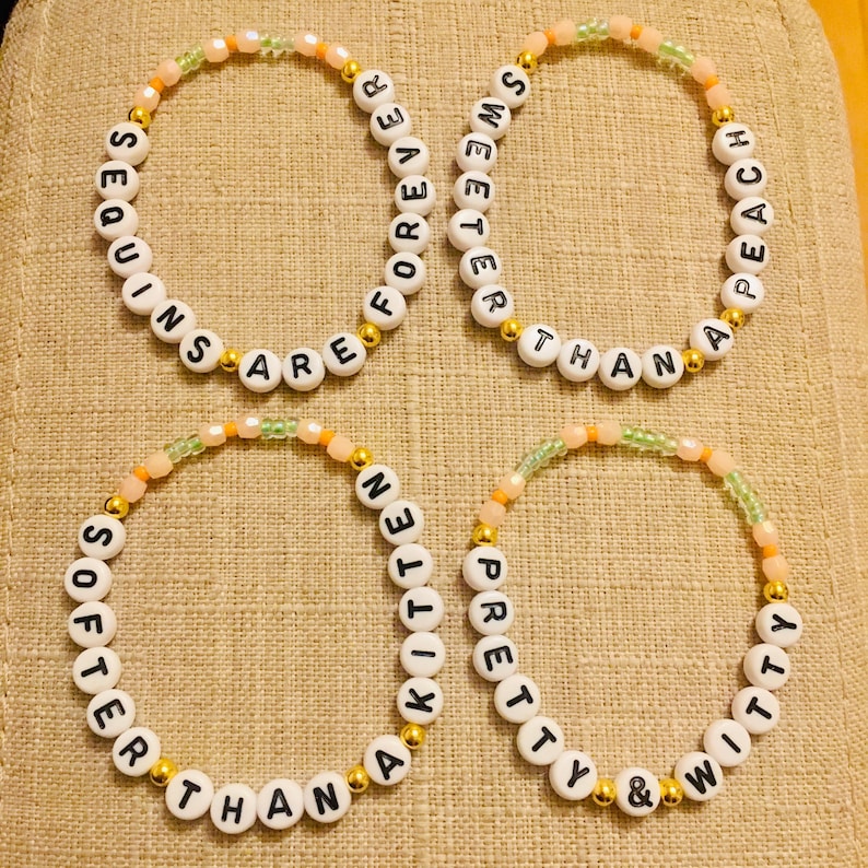 May include: Four beaded bracelets with white letter beads spelling out phrases like "Sequins are forever" and "Sweeter than peach." The bracelets have gold and pastel-colored accent beads.