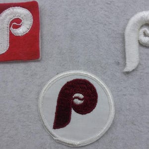 May include: Three embroidered patches featuring the letter "P" in different styles. One patch is red with a white "P", another is white with a maroon "P", and the third is white with a white "P" in a curved shape.