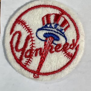 May include: Embroidered patch featuring the New York Yankees logo. The patch is circular, with a white background and a red outline. The team name is in red script, and a blue and red hat is in the center. The patch measures approximately 2.5 cm in diameter.