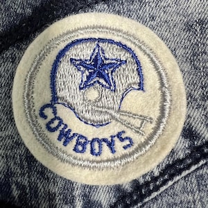 May include: A white patch with a blue star inside a gray helmet and the word "COWBOYS" in blue embroidery.