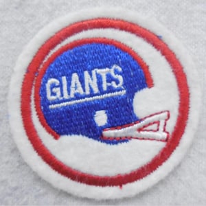 May include: A white, red, and blue embroidered patch with the word "GIANTS" in white lettering on a blue helmet. The patch is surrounded by a red circle.