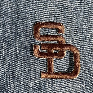 Può includere: Toppa ricamata marrone con le lettere "SD" su uno sfondo in denim blu.