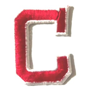 May include: A red, plush letter "C" patch with a white border. The letter is a bold, block style, and the edges are slightly rounded. The patch is likely for apparel or crafts.