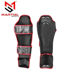 May include: Black and red shin guards with the "MARTIAL SPORTS" logo. The guards are made of a black material with red trim and straps for secure fastening. The design is for martial arts training and competition.