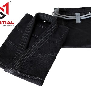 May include: Black martial arts uniform with a white drawstring on the pants and white stitching on the jacket. The jacket is folded and the pants are laid out flat. The logo "MARTIAL SPORTS" is visible in the top left corner.