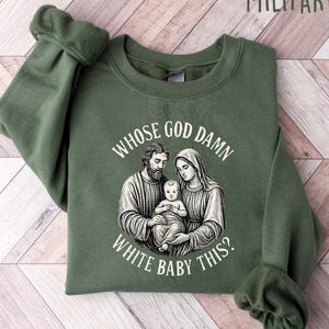 May include: Military green sweatshirt with the text "WHOSE GOD DAMN WHITE BABY THIS?" and a black and white graphic of a religious family. The sweatshirt has long sleeves and a crew neck.