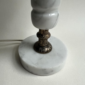 May include: A small, decorative lamp with a white marble base and a white marble lamp shade. The lamp has a bronze-colored, ornate base and a power cord. The lamp is a decorative home accent.