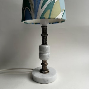 May include: A small table lamp with a marble base and a patterned lampshade. The lamp features a white and gray marble body with bronze-colored metal accents. The lampshade has a blue, green, and white abstract design.