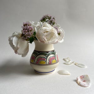 May include: A white ceramic vase with a colorful geometric pattern, filled with white roses and purple flowers.